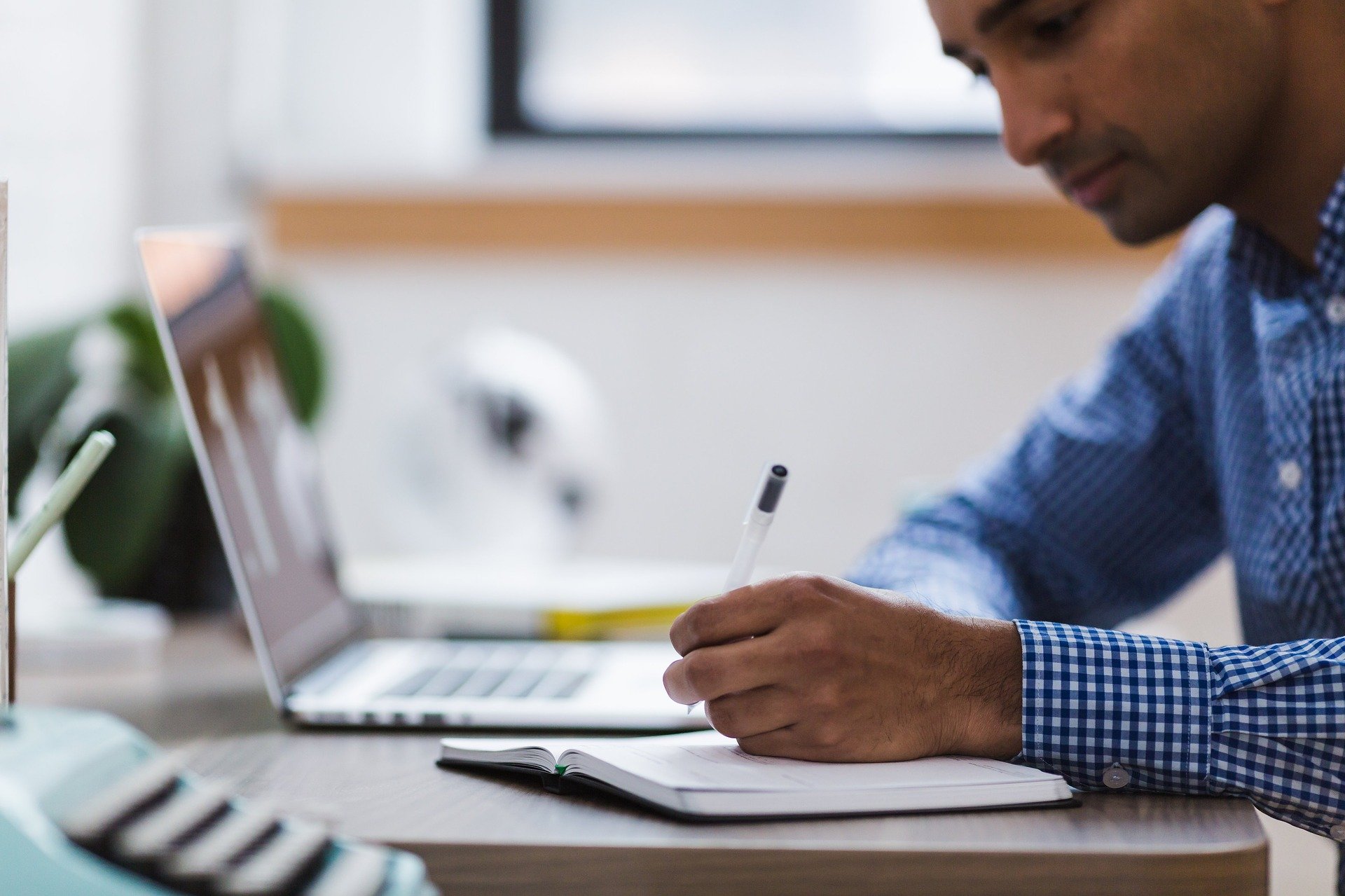 A man taking notes next to a laptop.